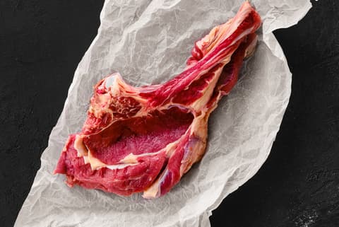 Vista superior d'un bistec de costella cru amb os sobre paper blanc arrugat en un fons fosc.